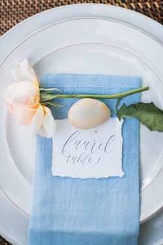 a place setting with a napkin and flower on it, along with a name tag