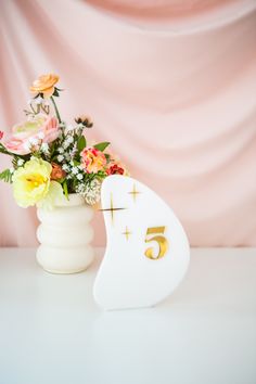 a white vase filled with flowers next to a number five sign on a table top