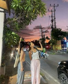 two women standing next to each other on the side of a road at night with their hands up in the air