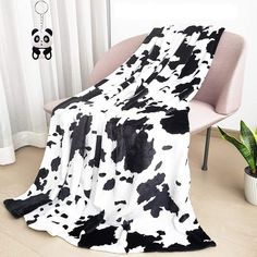 a black and white cow print blanket sitting on top of a chair next to a potted plant