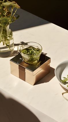 A steaming bowl of green tea in morning sunlight next to a plate of flowers on a marble surface with gold accents. Green Bowl, Vibrant Flowers