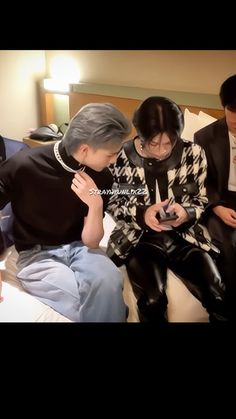 three people sitting on a bed looking at their cell phones while one person looks down