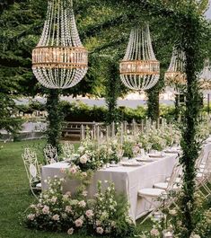 an outdoor dining area with chandeliers and flowers on the table, surrounded by greenery