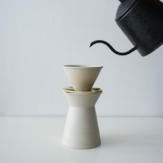 a black coffee pot and two white cups sitting on top of each other