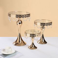 three pieces of gold colored tableware on a white table with a cup and saucer