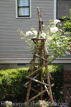 a tree made out of sticks and branches in front of a house with white flowers