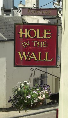 a red sign that says hole in the wall with flowers hanging from it's side