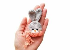 a hand holding a tiny crocheted bunny in it's right hand and wearing a scarf around its neck