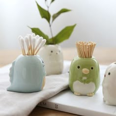 three small ceramic animals sitting on top of a white table next to a green plant