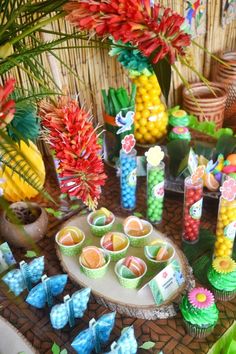 a table topped with cupcakes covered in candy next to flowers and pineapples