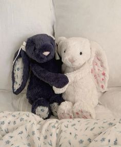 two stuffed animals sitting next to each other on a bed