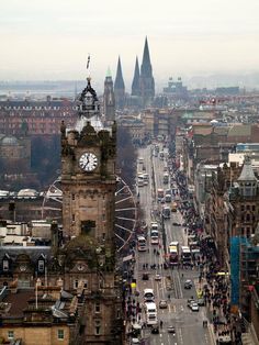 a large clock tower towering over a city filled with tall buildings and traffic on a cloudy day