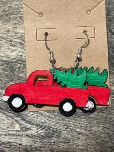 a pair of wooden earrings with a red car carrying a christmas tree on it's back