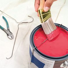 a person is using a brush to paint a red bucket with some scissors on it