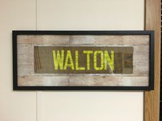 a wooden sign with the word walton written on it in yellow paint and black frame