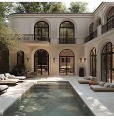 an outdoor swimming pool in front of a large white house with lots of windows and doors