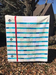 a blue and white striped quilt hanging from a tree in front of a house with leaves on the ground