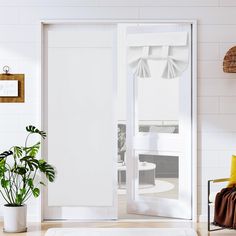 a living room with white walls and wooden flooring, two planters on either side of the glass door