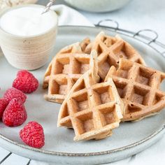 three waffles on a plate with raspberries and yogurt in the background