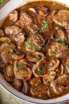 a pan filled with mushrooms and gravy on top of a wooden table