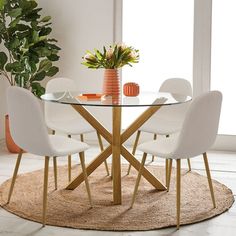 a glass dining table with white chairs and a potted plant on the rug in front of it