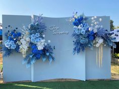 two blue and white flowers are hanging on the side of a wall that says happy birthday