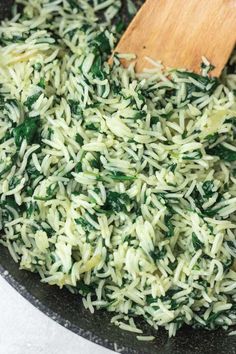 rice and spinach being cooked in a skillet with a wooden spatula on the side