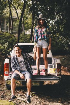 two people standing on the back of a pick up truck with trees in the background