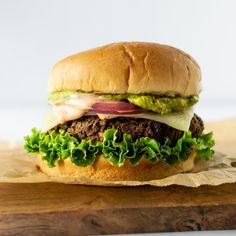 a hamburger with lettuce, tomato and onion on a wooden cutting board next to a knife