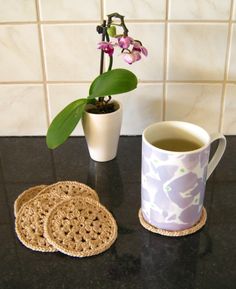 a cup of tea next to two coasters with flowers in them on a counter