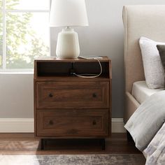 a nightstand with a lamp on top of it next to a bed and a window