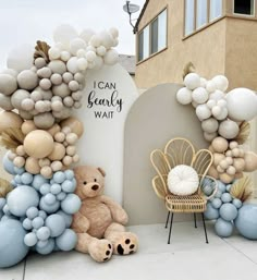 a teddy bear sitting in front of a bunch of balloons on the ground next to a chair