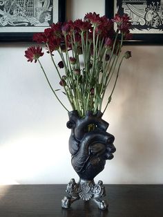 a vase filled with red flowers sitting on top of a wooden table next to two framed pictures