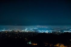 the city lights are lit up at night from atop a hill in the distance is a foggy sky