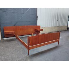 a wooden bed frame sitting on top of a cement floor next to a metal wall