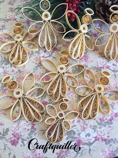 six wooden angel ornaments sitting on top of a flowery tablecloth with pine cones in the background