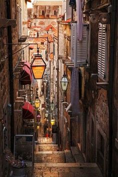 two people sitting on a stone bench in an alleyway with lots of hanging lights