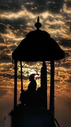 the silhouette of a person sitting under a gazebo at sunset with clouds in the background