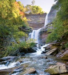 a waterfall in the middle of a forest with rocks and trees on either side of it