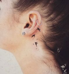 a woman's ear with birds and stars behind her left ear, on the side of her right ear