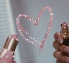 a person holding a pink lipstick in their hand and a heart shaped bottle with glitter on it