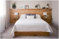 a bed with white linens and pillows in a bedroom next to a wooden headboard