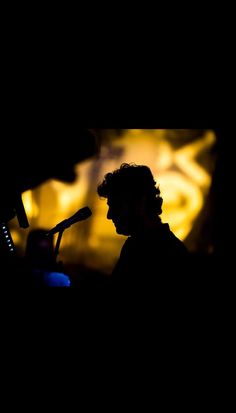 the silhouette of a man speaking into a microphone in front of a screen with yellow lights