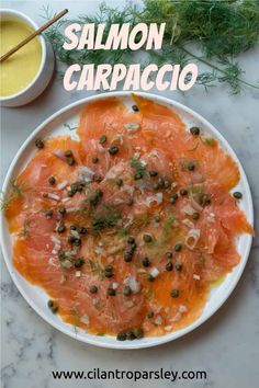 salmon carpaccio with capers and dill on a white plate next to a bowl of mustard