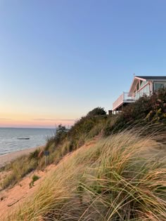 a house on the side of a hill next to the ocean with grass in front of it