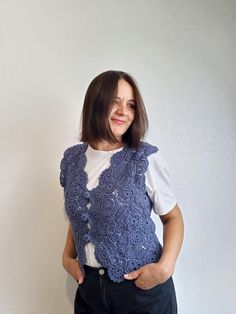 a woman standing in front of a white wall wearing a blue crochet vest