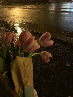 pink tulips are in a vase on the side of the road at night