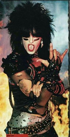 a woman with black hair and piercings making the peace sign while wearing punk clothing