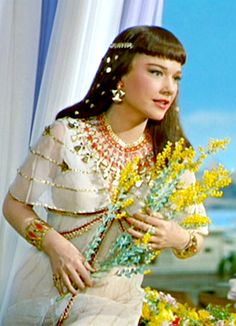 a woman in a white dress holding yellow flowers and wearing an elaborate head piece with pearls