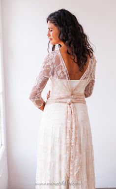 the back of a woman wearing a white dress with lace sleeves and a bow at the waist